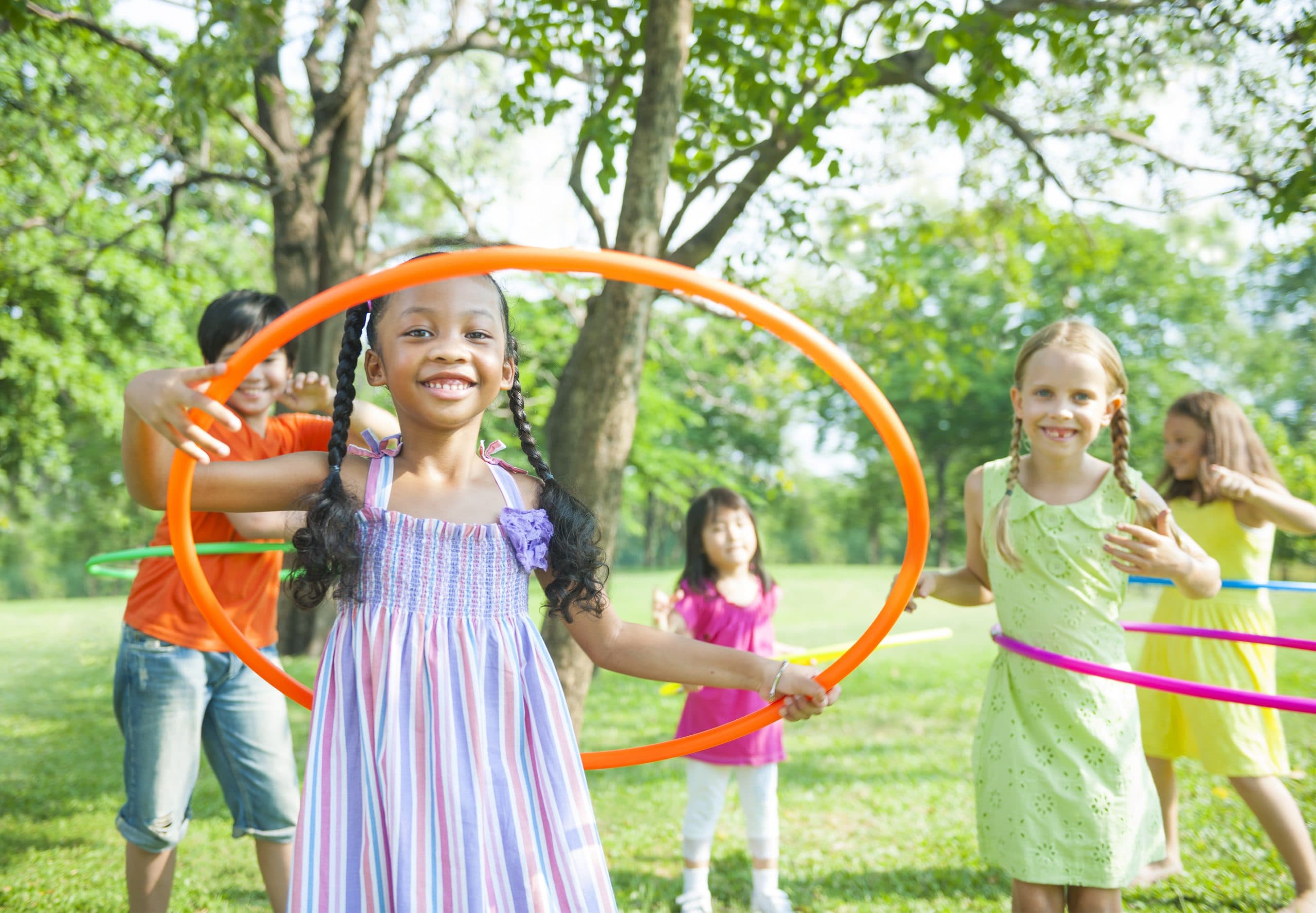 5 Children Playing with hula hoops in a field with trees in the foreground.